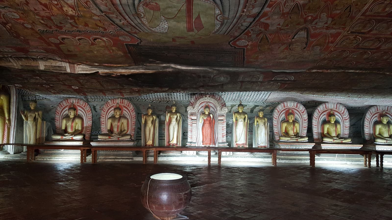 Reihen von Buddha-Statuen unter der bemalten Decke einer Höhle in Dambulla