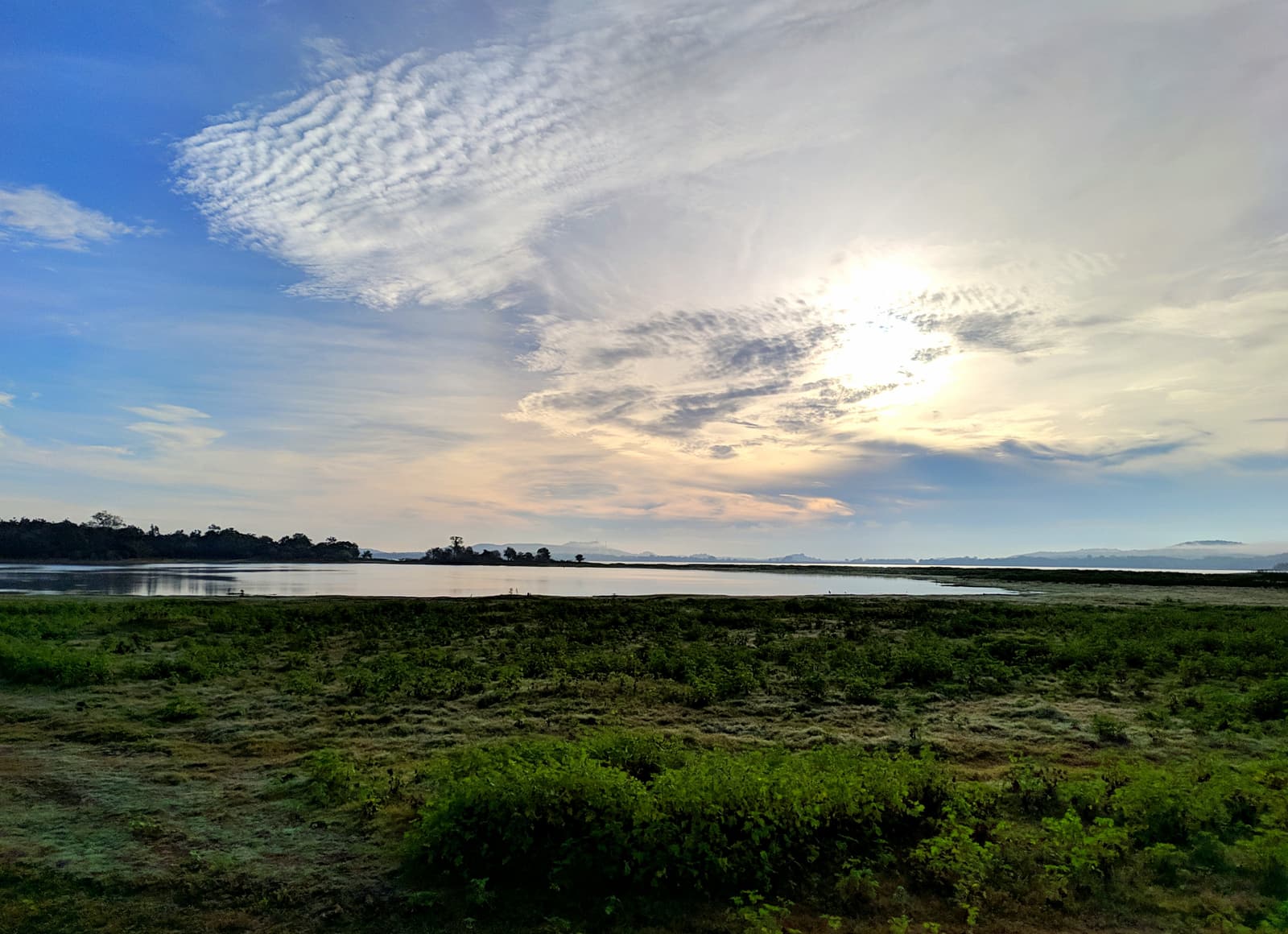 Der weite Minneriya-Stausee unter dramatischem Himmel, im Vordergrund Grasland